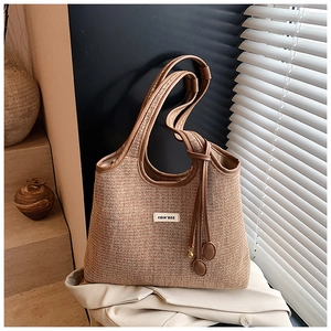 Detailaufnahme einer gestreiften Strohtasche mit braunen Ledergriffen und Markenlogo