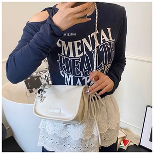 Detail of beige crossbody bag featuring silver chain strap and metal bow charm detail