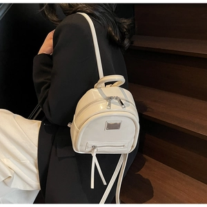Detail view of the mini cream leather backpack showing glossy finish and silver metal logo