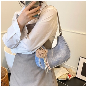Detail of light blue denim half-moon shoulder bag with a brown plush bear charm