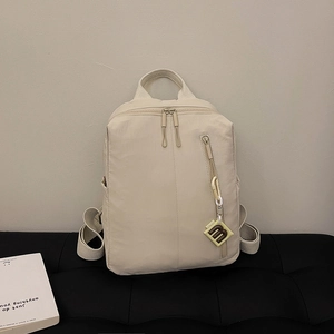 Macro shot of beige nylon backpack featuring side pockets and a stylish letter m pendant