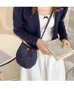 Détail du sac à bandoulière en denim bleu avec broderies de cerises et de nœuds rouges