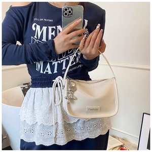 Detail of cream white shoulder bag with glossy finish and silver balloon dog charm