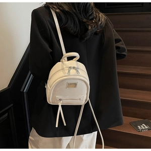 Detail of a creamy white mini leather backpack with metallic plate on a model's back