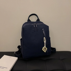Detail of navy blue nylon backpack with decorative charm on a black textured bench