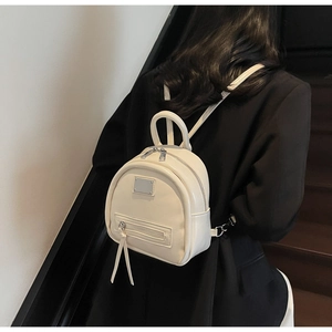 Rear view of a cream mini fashion backpack on a model in a minimalist setting
