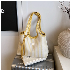 Detail of yellow and white striped canvas tote bag with leather handles on a silver suitcase