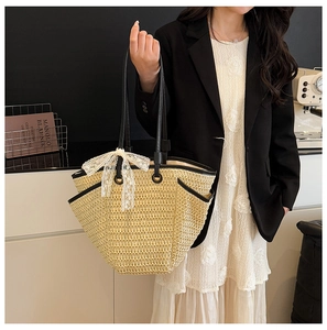 Détail d'un sac cabas en paille tressée beige avec nœud en dentelle et anses noires