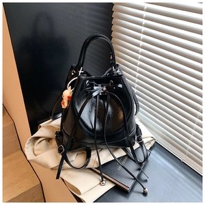 Detail of black glossy PU leather bucket bag with bow drawstring and white rabbit charm