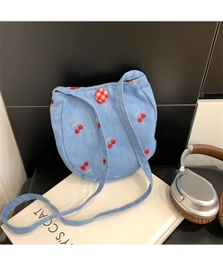 Détail d'un sac à bandoulière en denim bleu clair avec broderie cerise et bouton à carreaux