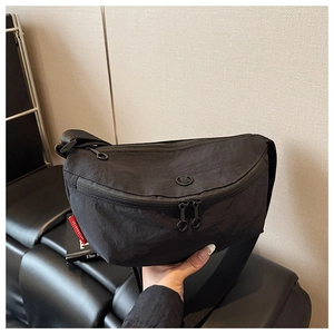 Detail of minimalist black nylon crescent chest bag featuring dual zippers and woven label
