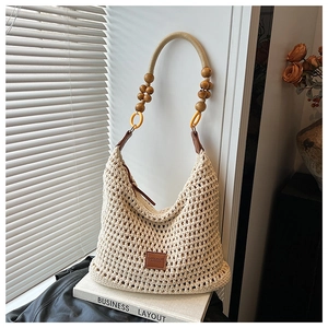 Detail of a beige woven hobo bag with wooden beads and leather patch on books