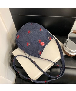 Détail d'un sac bandoulière en denim bleu avec broderie cerise et un bouton à carreaux