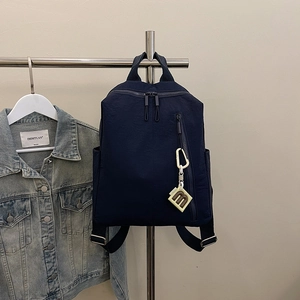 Detail of navy blue nylon backpack with dual zippers and decorative logo tag on a hanger