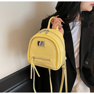 Close-up of bright yellow patent leather mini backpack with silver zippers and top handle