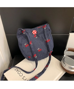 Détail d'un petit sac bandoulière en denim bleu foncé avec broderies cerises et bouton