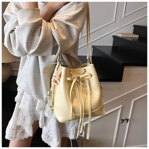Detail of pale yellow drawstring bucket bag with cute bear charm and leather bow