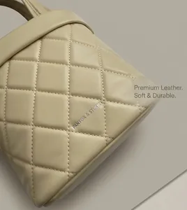 Dettaglio della pelle trapuntata beige e del logo argentato sulla borsa a secchiello
