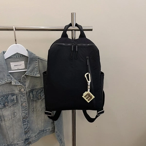 Detail of black textured fabric backpack featuring a side zipper and decorative m-pendant