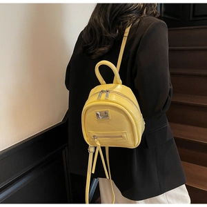 Rear view of a model wearing a bright yellow shiny PU leather mini backpack on a white wall