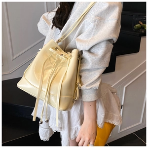Detail of beige bucket backpack with drawstring closure and silver ball charms on a model