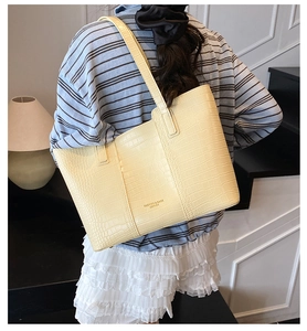 Crocodile pattern leather texture and brand lettering detail on cream tote bag