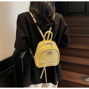 Detail of bright yellow faux leather mini backpack with glossy finish and silver logo plate