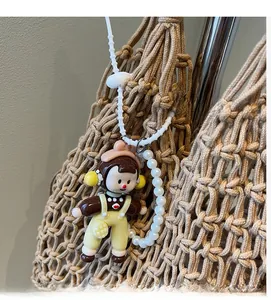 Detail of cute doll charm with pink bow and pearls hanging on a woven beige tote bag