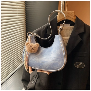 Detail of light blue denim hobo bag with silver strap and cute brown bear charm