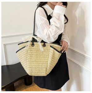 Détail du sac cabas en paille avec bandoulières noires et un grand nœud en dentelle blanche