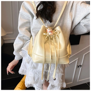 Detail view of cream bucket backpack featuring decorative leather bow and panda charm