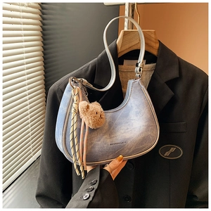 Detail of light blue denim half-moon underarm bag with plush bear charm and woven tassels