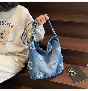 Detail of blue denim tote bag with frayed letter patches and wide shoulder strap