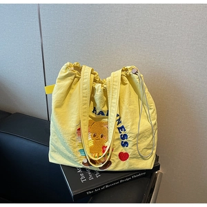 Detail of yellow nylon tote bag featuring blue HAPPINESS embroidery and plush bear pattern