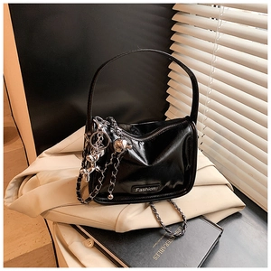 Detail of a black patent leather handbag with silver chain strap on a vintage book