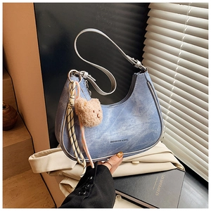 Detail of blue denim crescent hobo bag with teddy bear charm and adjustable leather strap