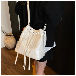Model wearing a white patent leather bucket bag with bow drawstring and metal beads