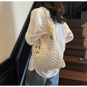 Detail of cream woven tote bag with hollow design, thick strap and a cute doll pendant