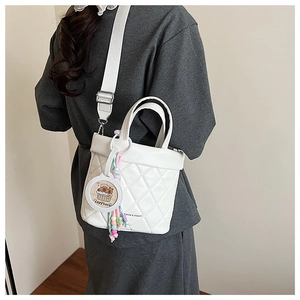 Detail of white quilted bucket bag with wide strap and cute capybara pendant charm