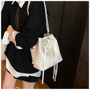 Detail view of white drawstring bucket bag with astronaut charm and smooth PU finish