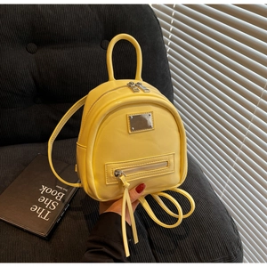 Detail of bright yellow mini PU leather backpack with gold metal plaque and long zipper pulls