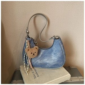 Blue denim hobo bag with a plush bear charm and striped ribbon on a vintage book