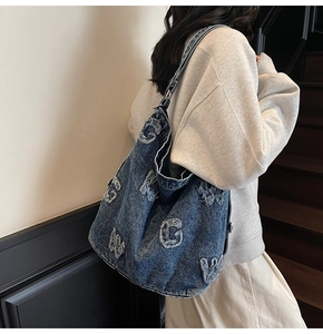 Detail of blue denim hobo bag featuring vintage letter patches and metallic buckle strap