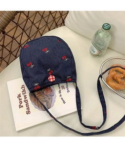 Détail du sac bandoulière en denim bleu avec broderie cerise et fermeture à bouton à carreaux