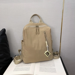 Detail view of khaki nylon backpack with fabric texture and letter 'm' charm on a book