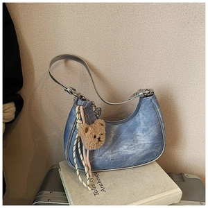 Close-up of blue denim hobo bag with silver trim and a cute brown plush bear charm