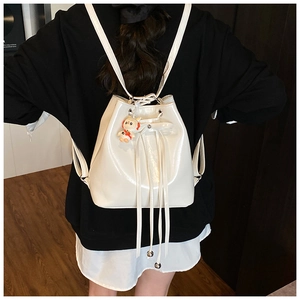 White patent leather bucket backpack featuring a rabbit astronaut charm on a model's back