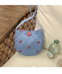 Détail du tissu denim bleu clair avec broderie cerise et bouton de fermeture à carreaux