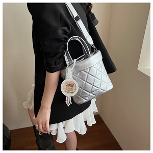 Detail of silver quilted bucket bag featuring a wide strap and capybara charm