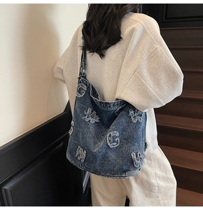 Detail of blue denim hobo bag featuring vintage frayed letter patches and crossbody strap